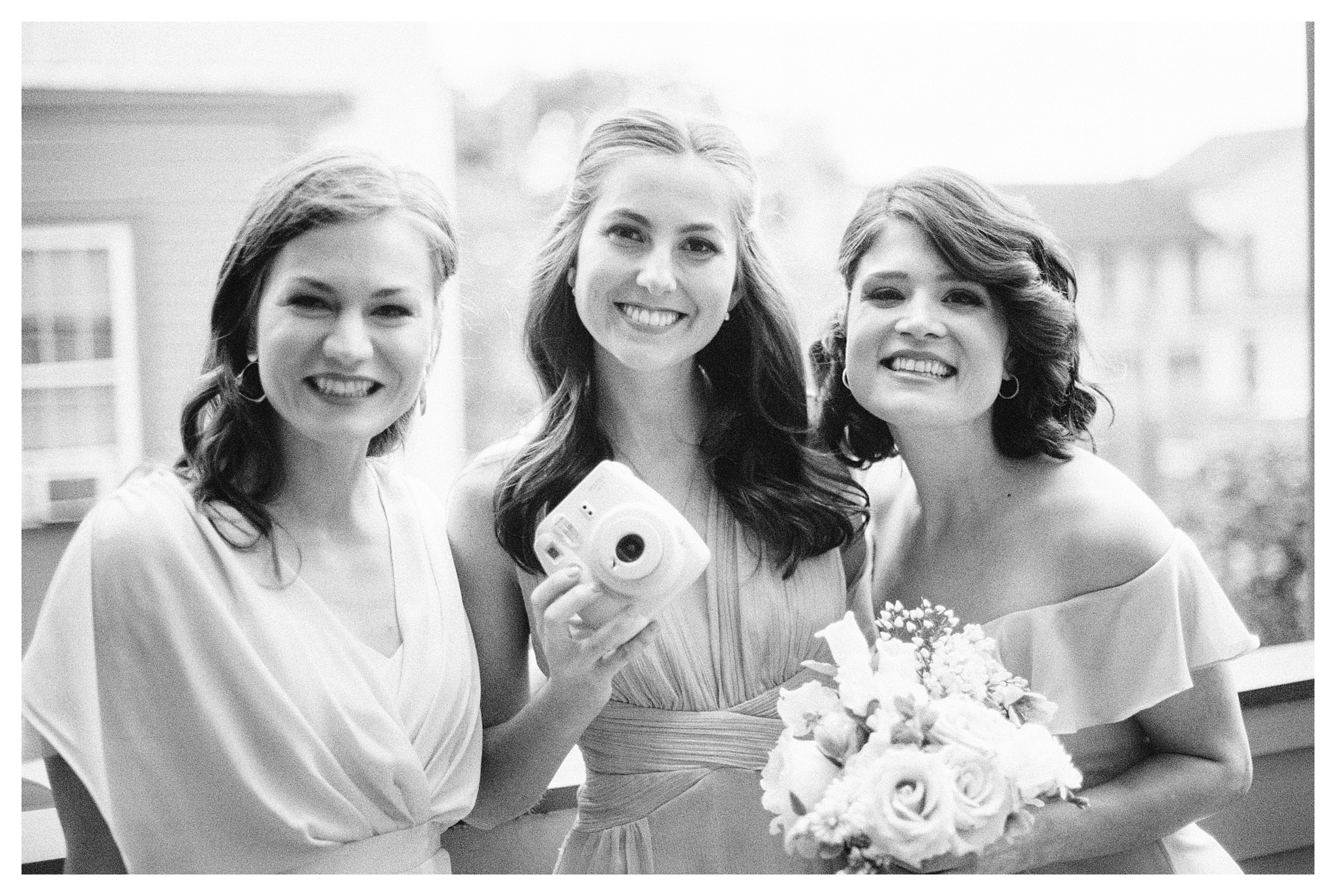 Bridesmaids hold an instant film camera and smile.