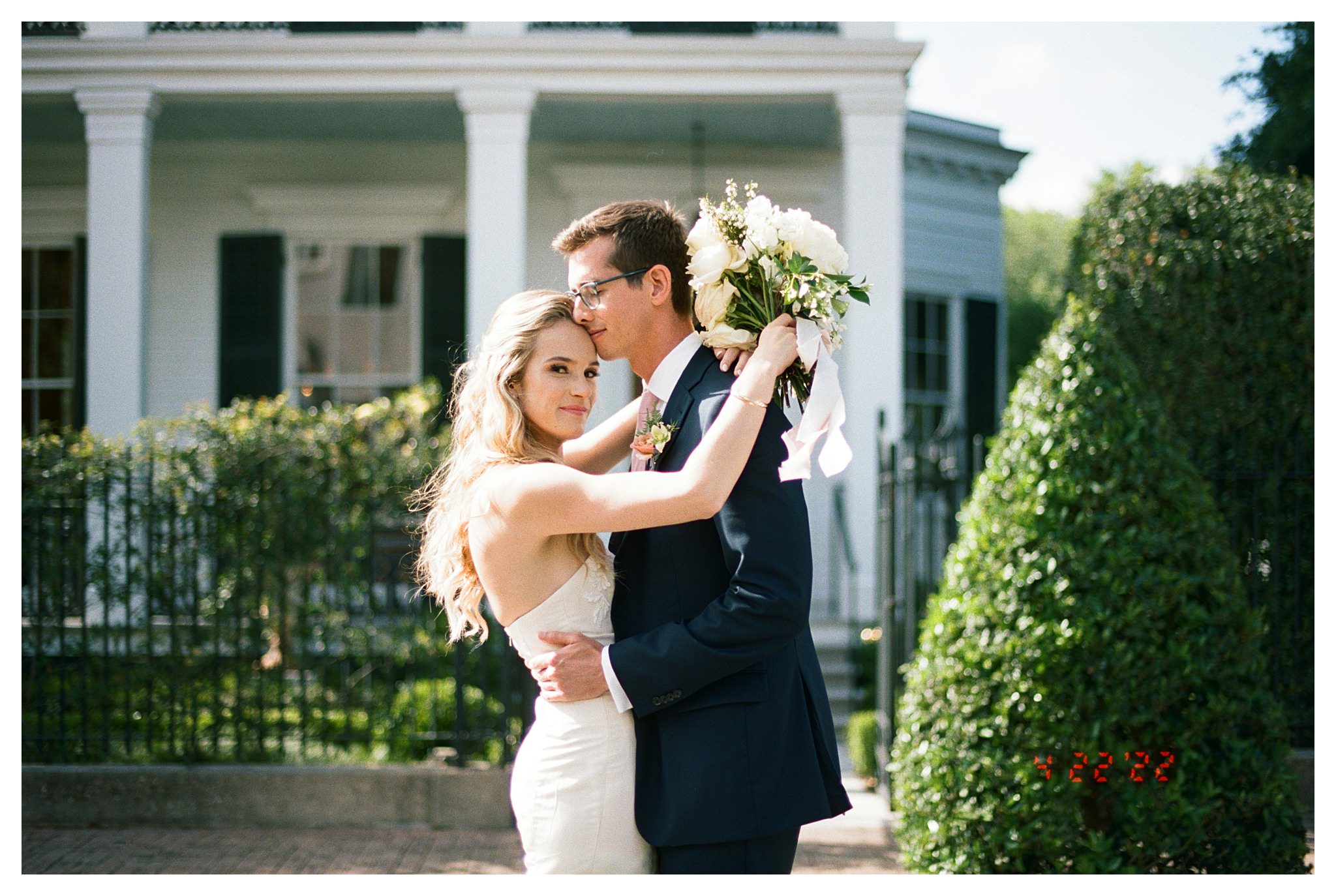 A couple stands in front of a White House for their New Orleans garden district wedding.