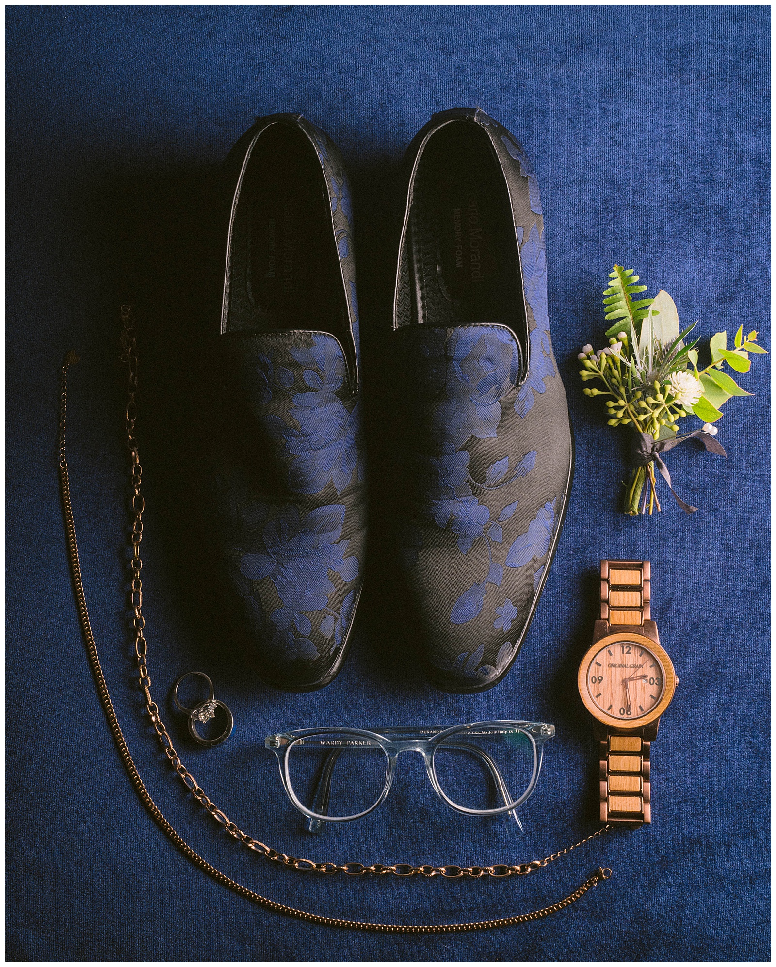 Blue shoes, glasses, and a bronze watch sit on a blue backdrop