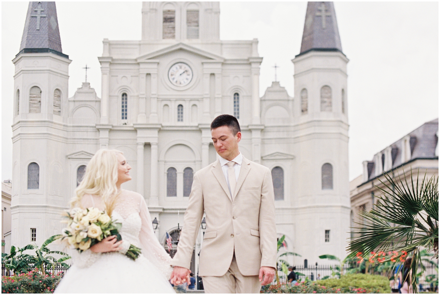 A man and woman stand in front of St. Louis Cathedral holding hands before their intimate wedding on film.