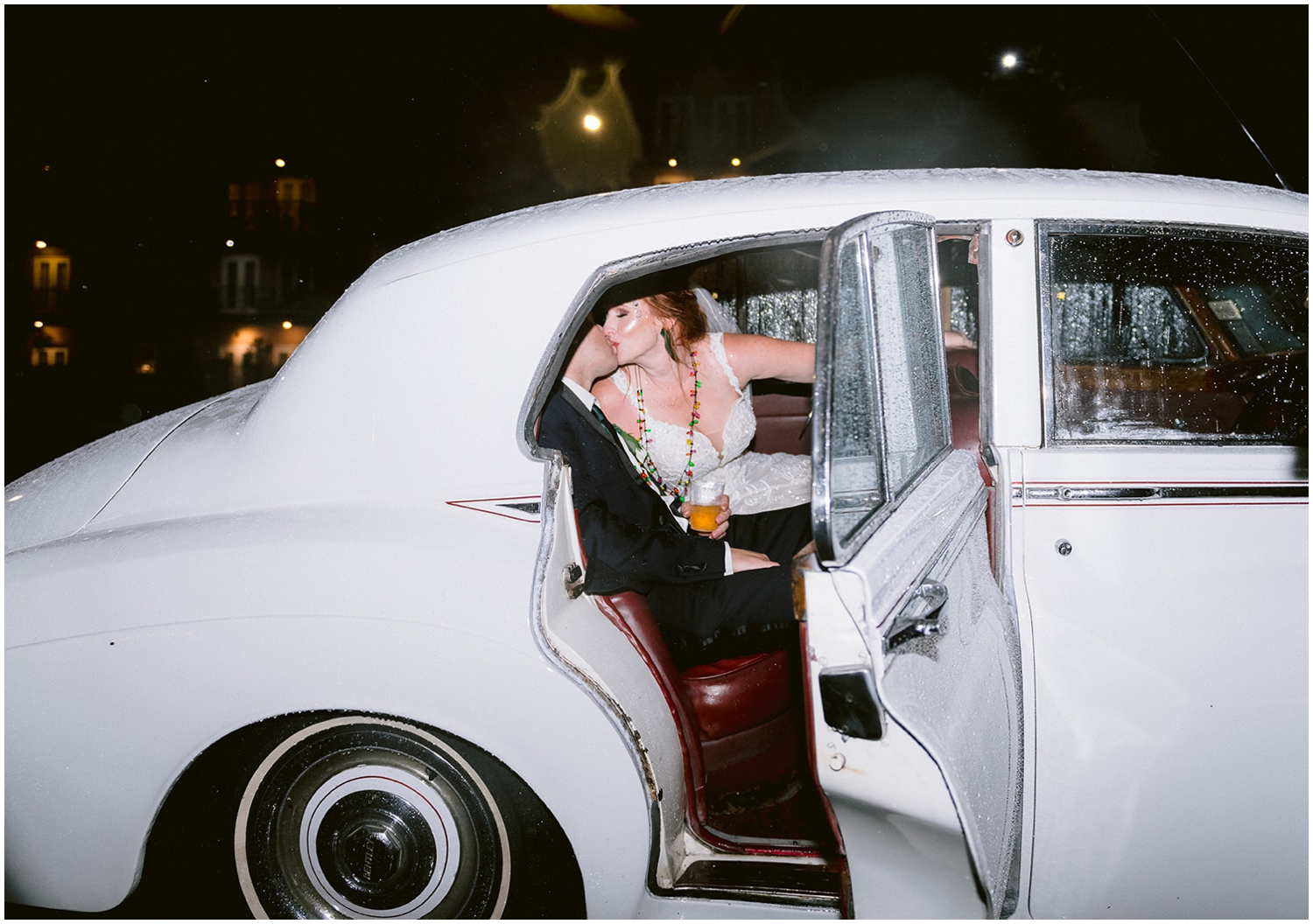 A couple kisses in the back seat of a car in direct flash for wedding photography.
