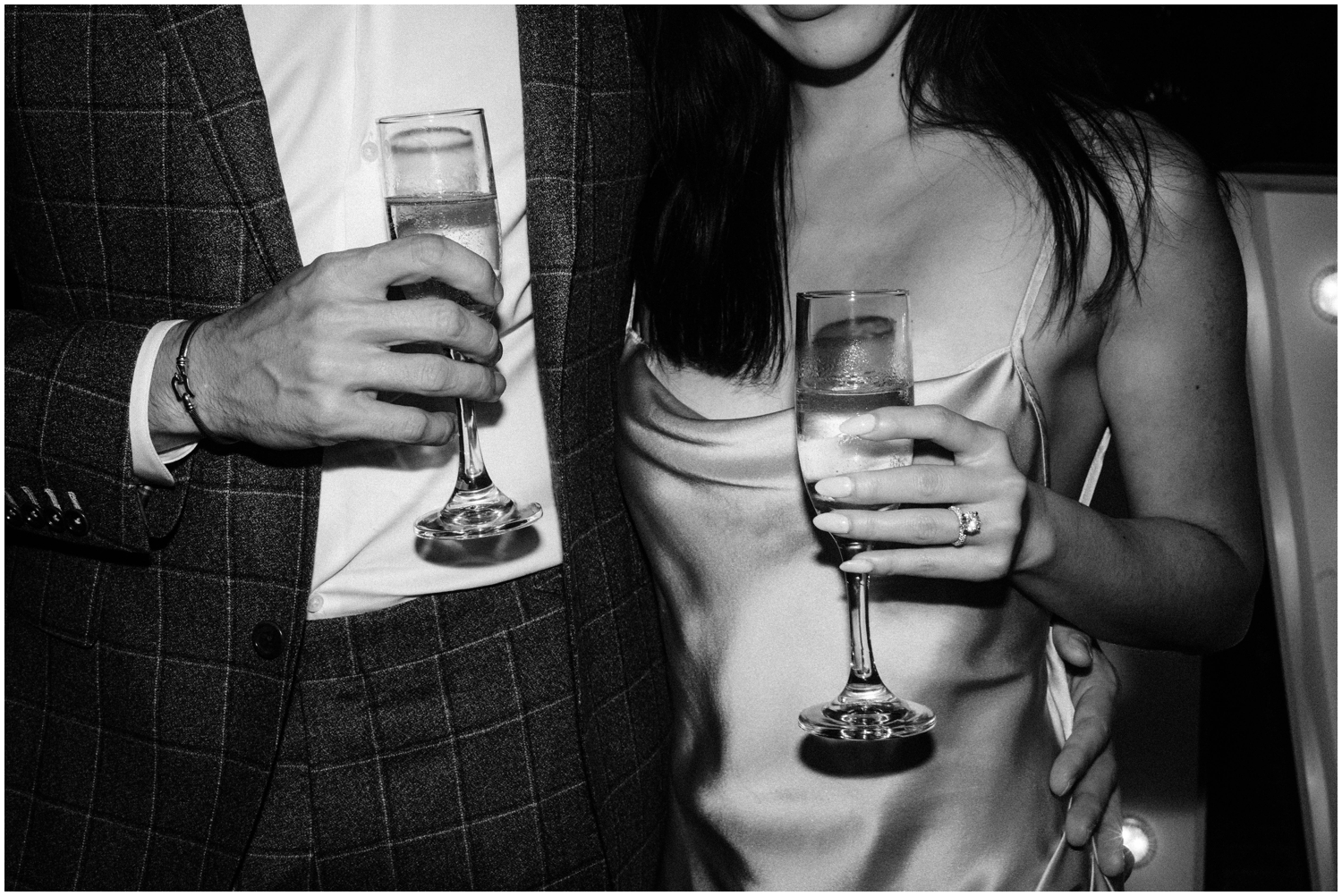 A direct flash photo shows a couple holding cocktails with an engagement ring.