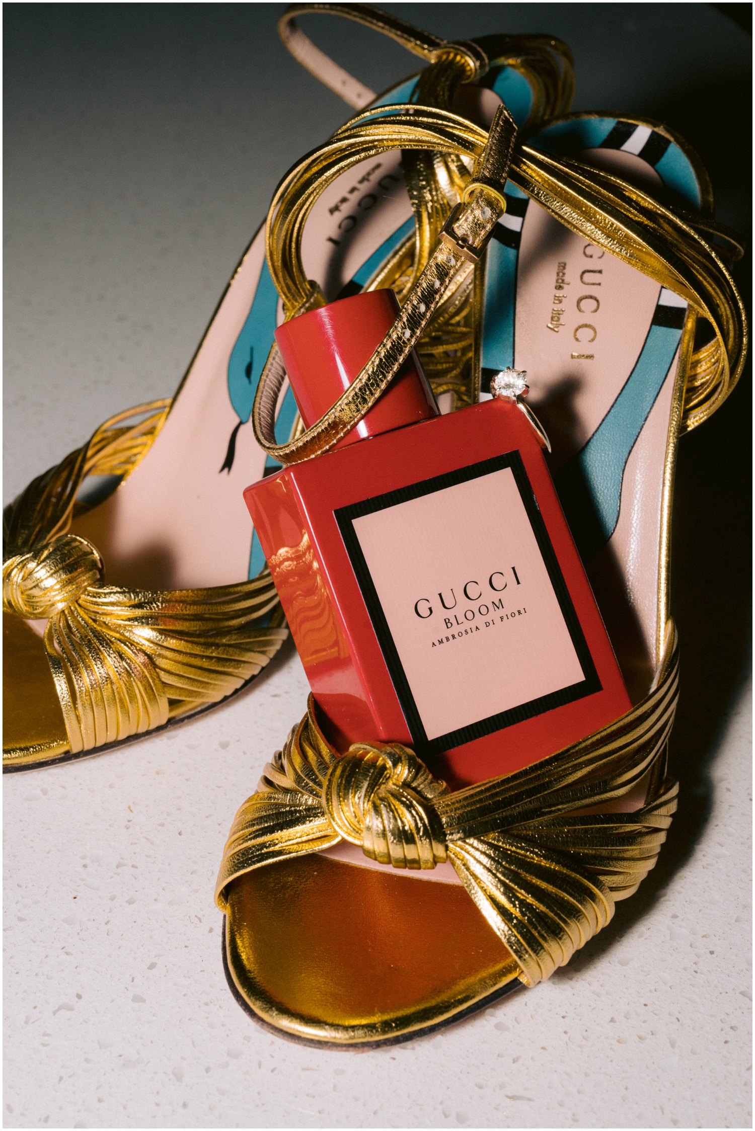 A red Gucci perfume bottle sits in a bride's gold Gucci heels.