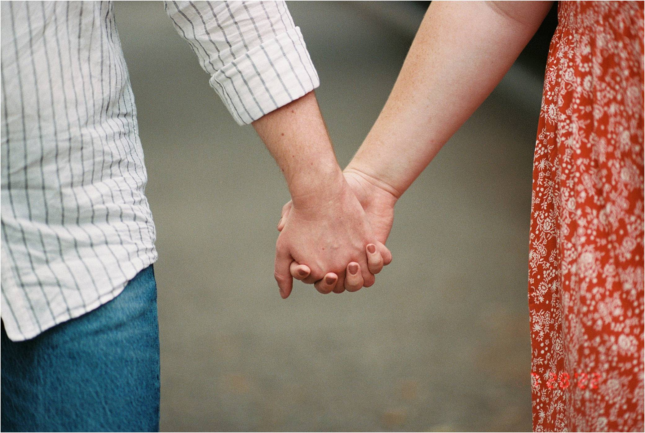 A man and a woman hold hands while walking through a park during an engagement session.