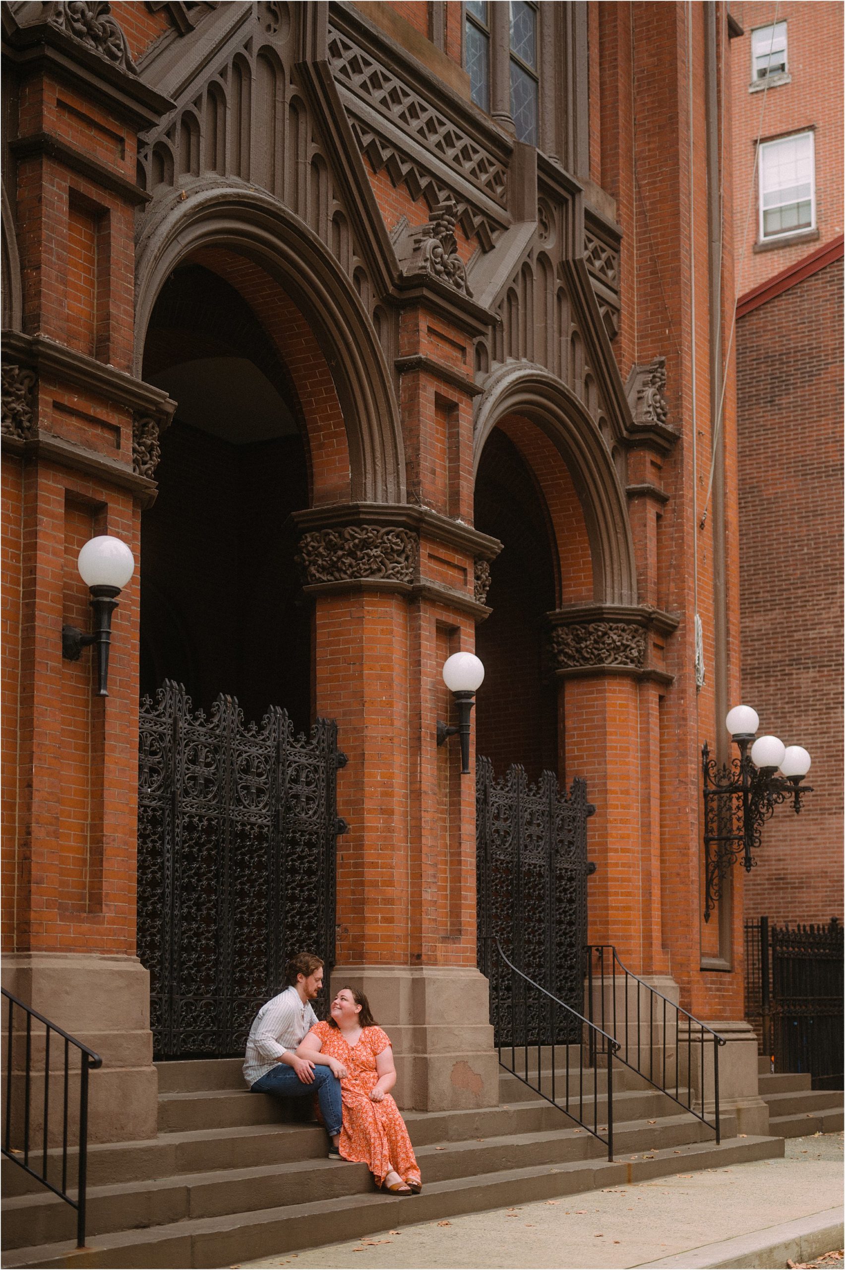 A man and woman sit on the steps of a brick building with black ironwork gates in the Rittenhouse neighborhood.
