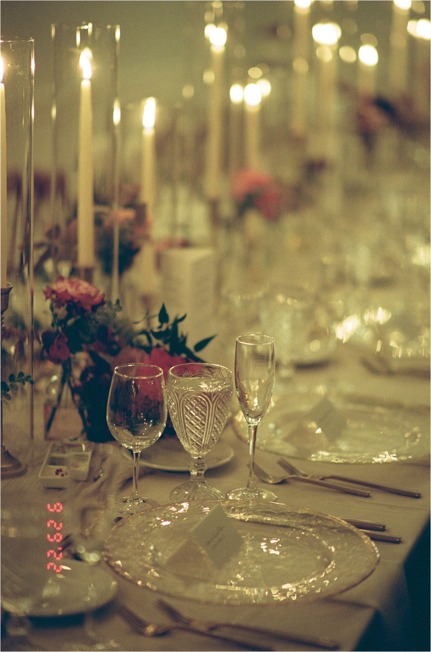 A film wedding photo shows glassware and florals set for a candlelit wedding reception.