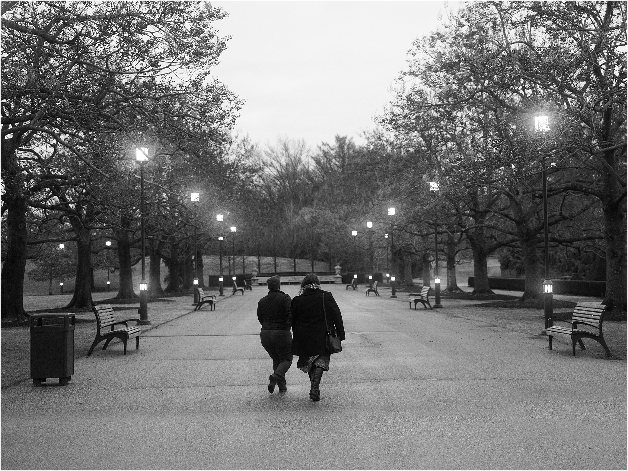A couple walks down the sidewalk of a Philadelphia park at dusk.
