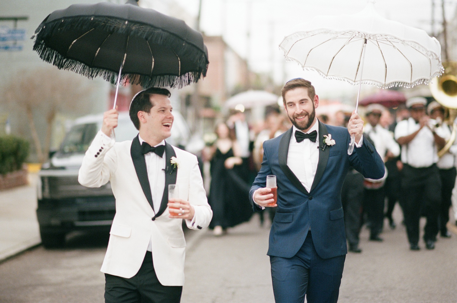 Two grooms carrying New Orleans wedding umbrellas lead a wedding second line through the French Quarter.