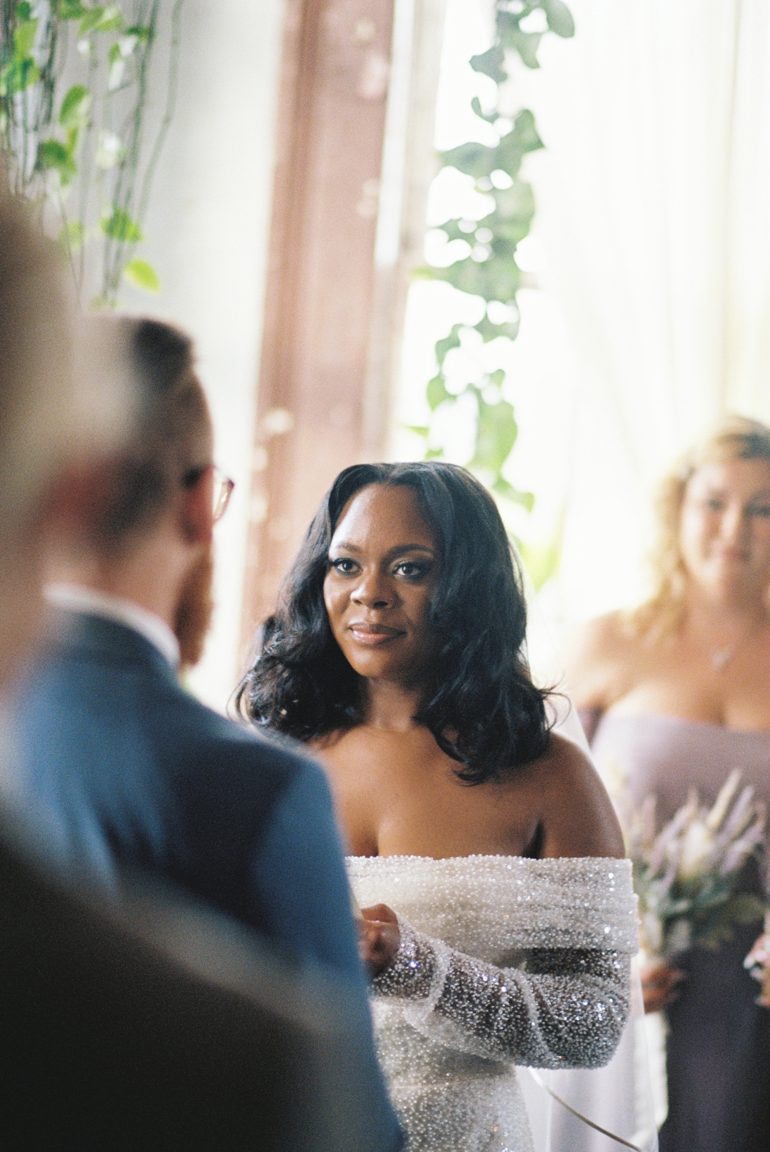 A bride in a beaded wedding gown listens to a groom read his vows at a Philadelphia wedding.