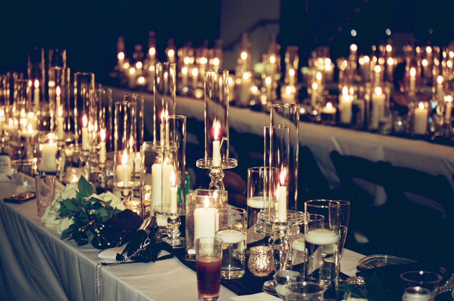Candles in glass holders line a wedding reception table in film wedding photography.