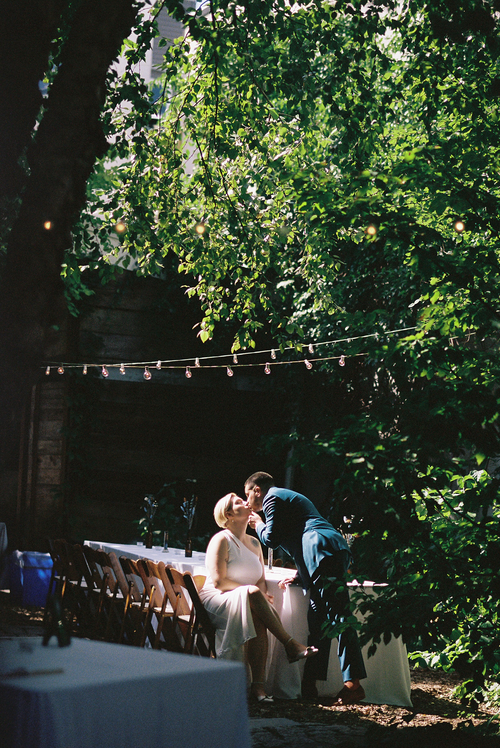 A marrier leans down and kisses a bride seated at a reception table in a Philadelphia wedding venue.