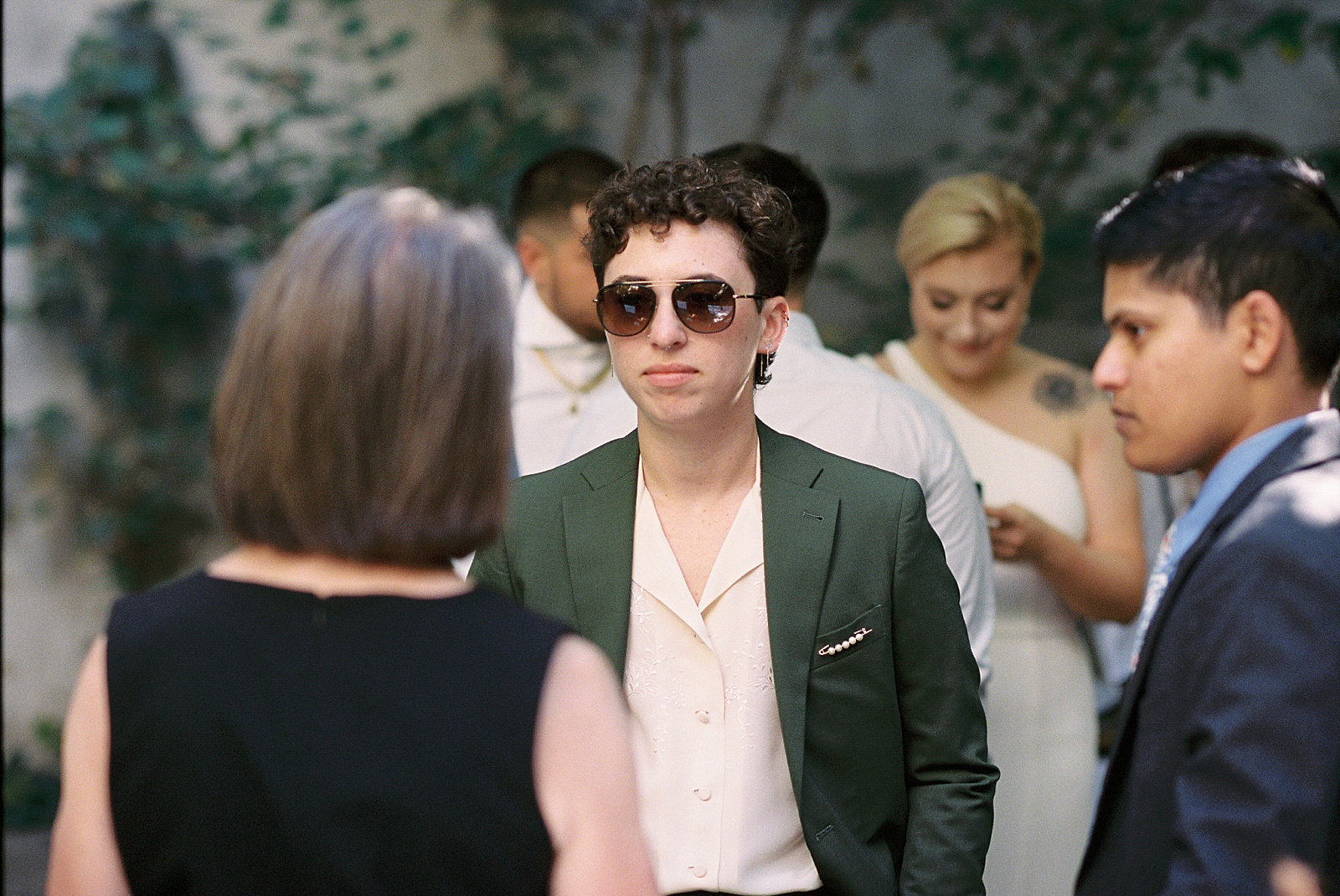 A wedding guest in a green suit wears sunglasses.