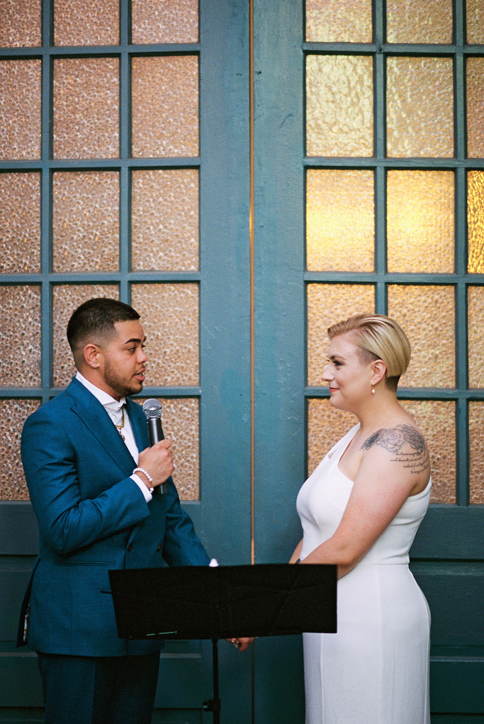A marrier says their vows into a microphone while a bride listens.