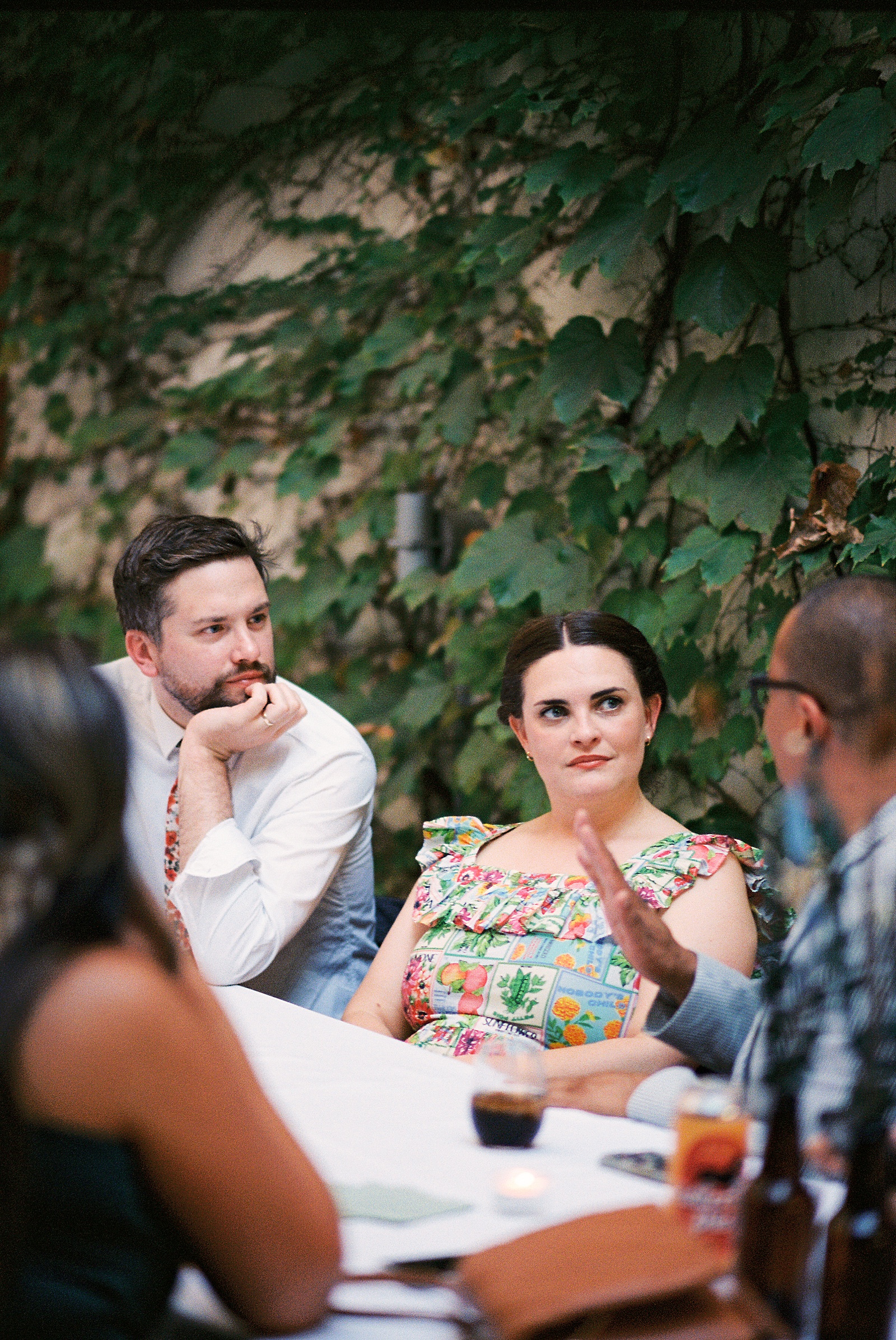 Wedding guests in floral print sit at a reception table in conversation.