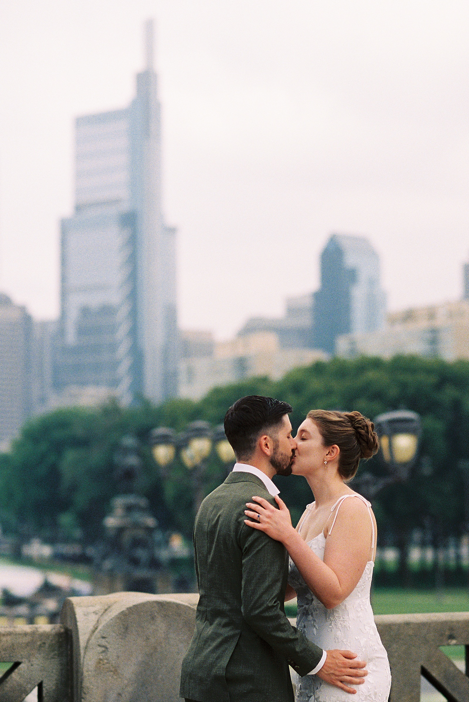 A bride and groom kiss in front of the Philadelphia skyline before their self-uniting ceremony at Fairmount Park.