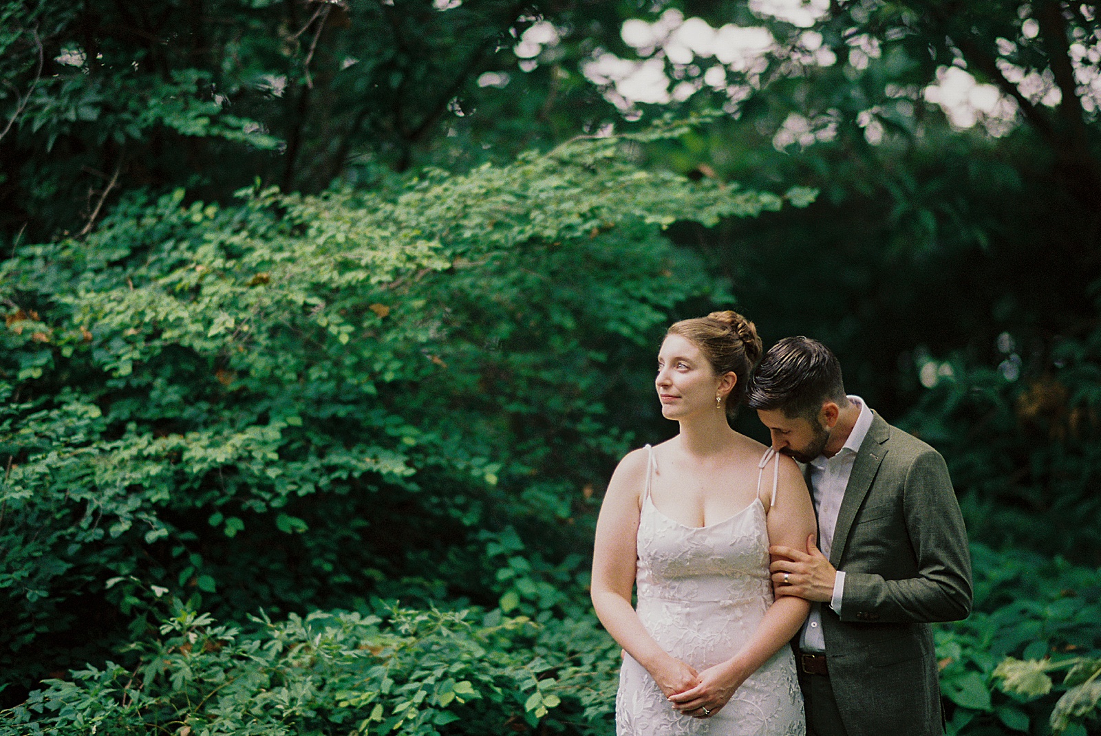 A groom kisses a bride's shoulder after their Philadelphia elopement ceremony in a park.