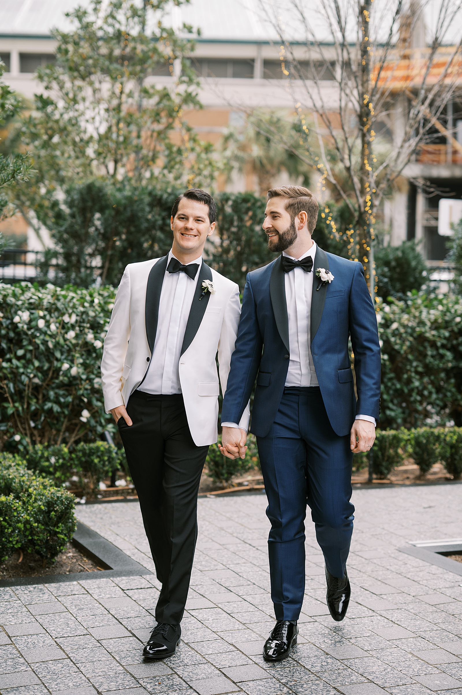 Two grooms hold hands and walk towards a film wedding photographer.