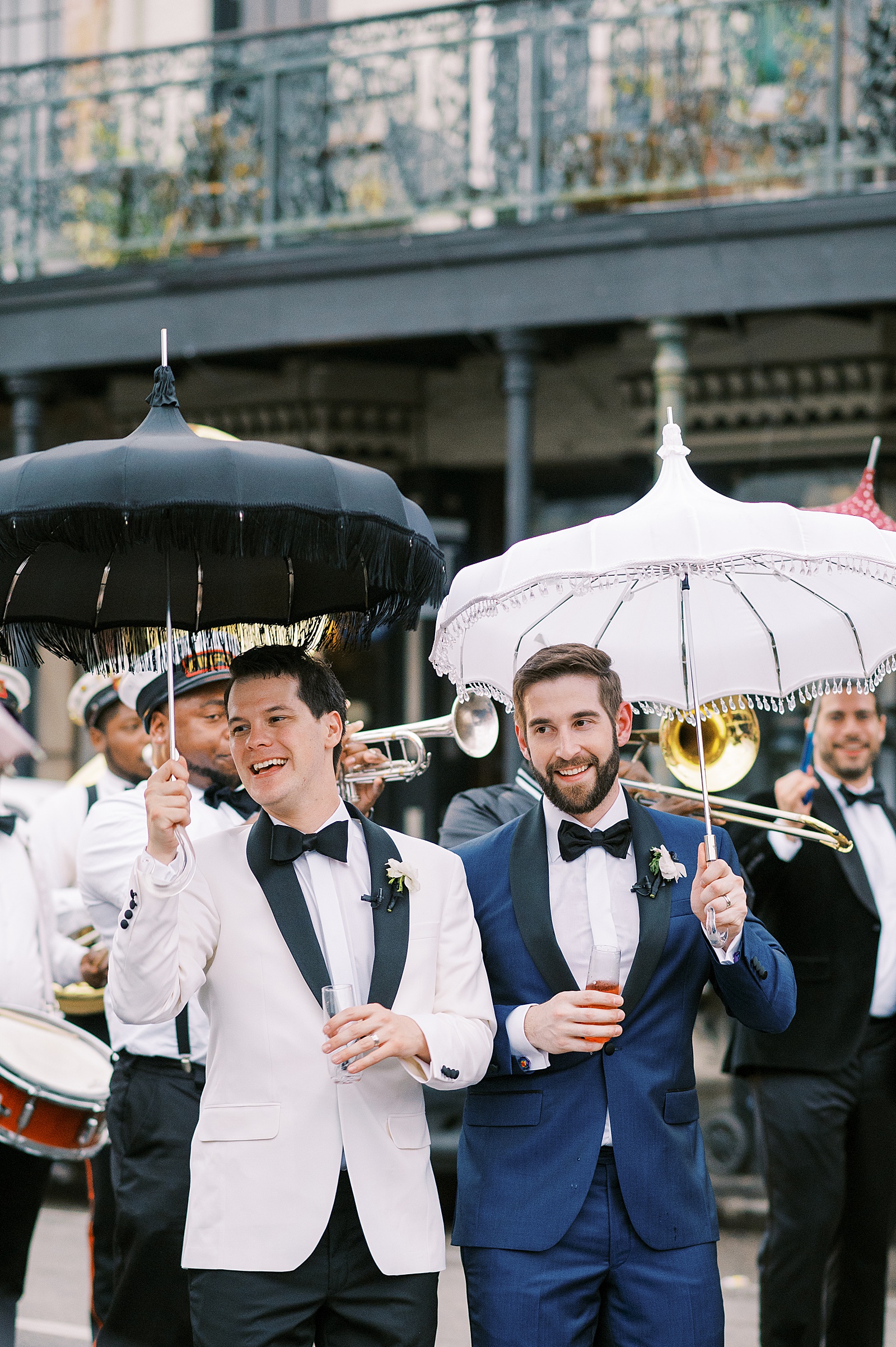 Two grooms stand side by side in a New Orleans street during a wedding second line.