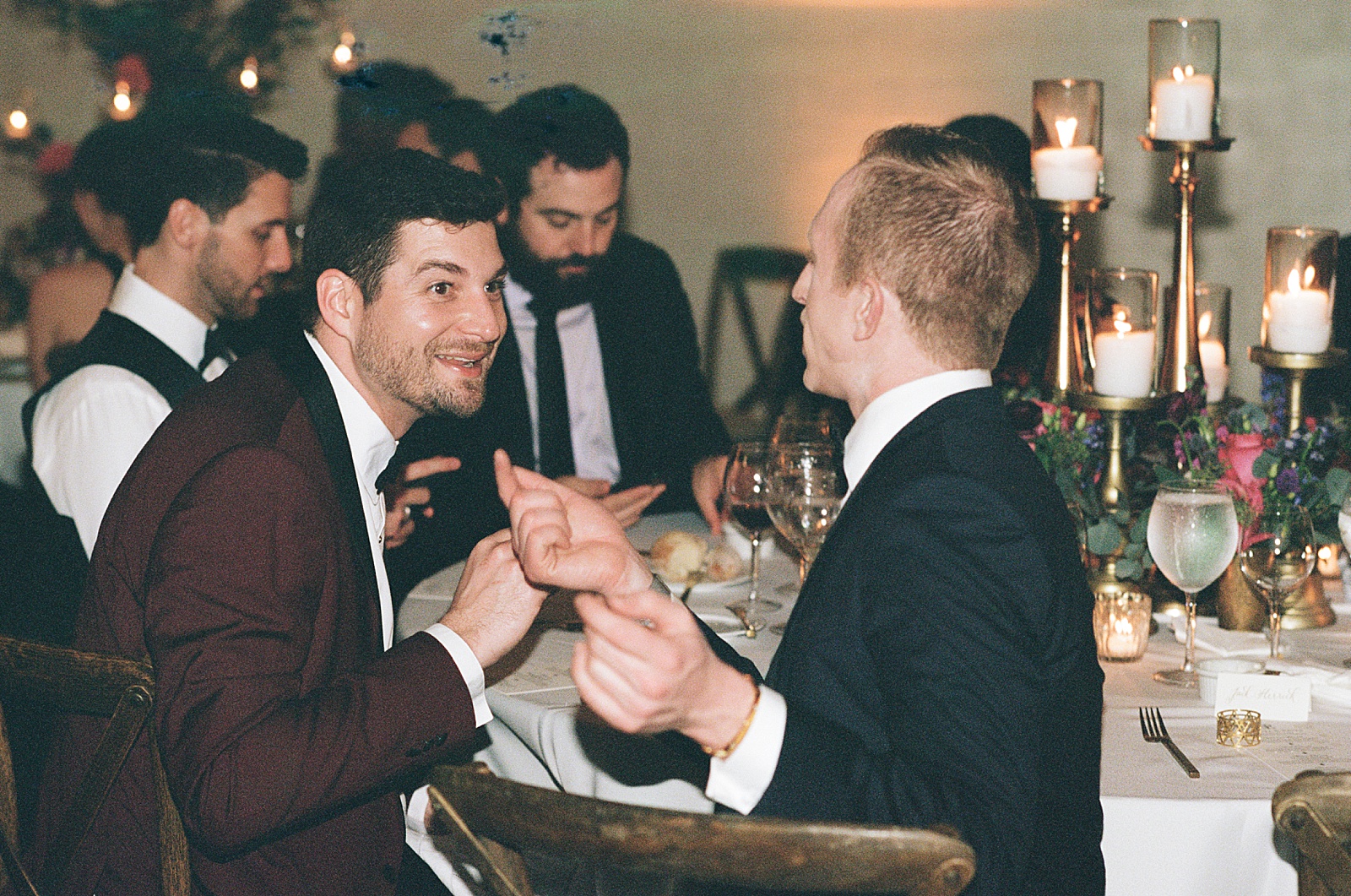 Wedding guests sit at reception tables and talk in a candid wedding photo on film.