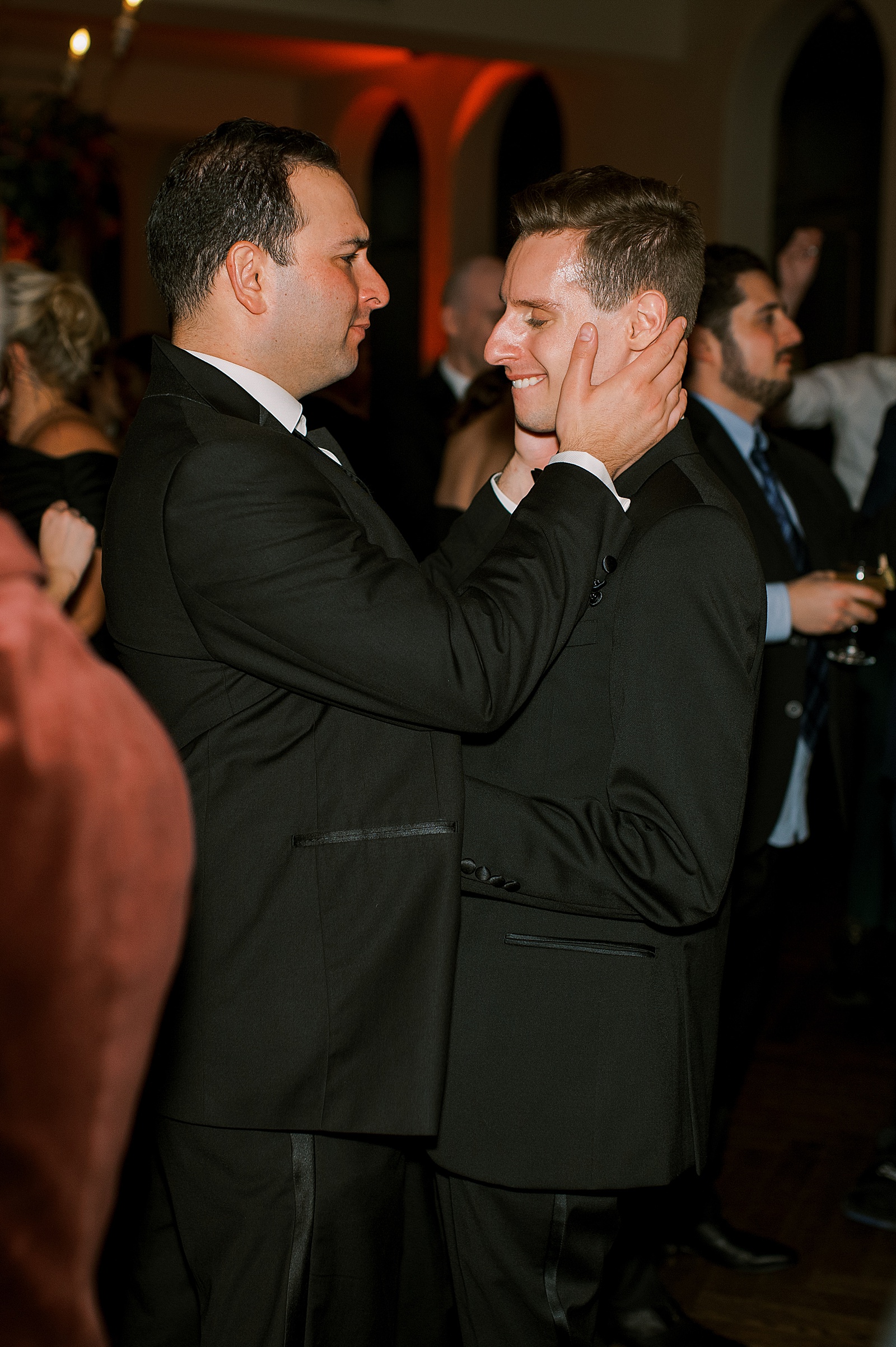 Two men embrace on the dance floor at a wedding reception.