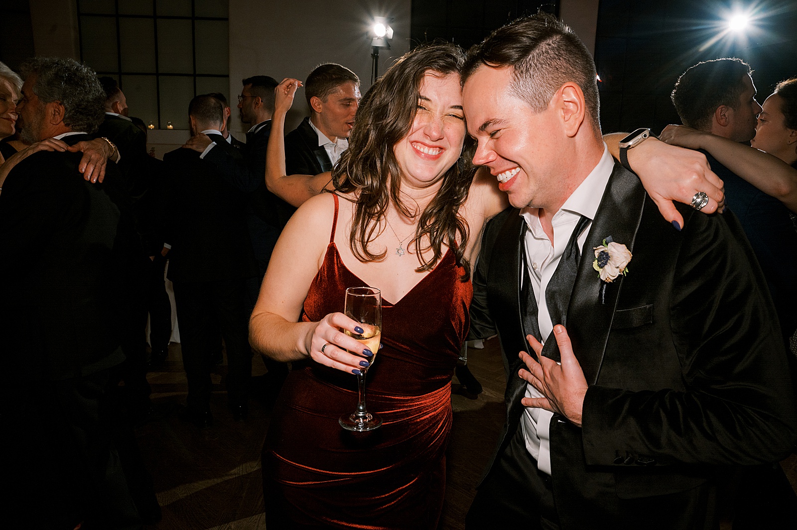 A man and woman lean on each other laughing on the edge of the dance floor of a wedding reception.