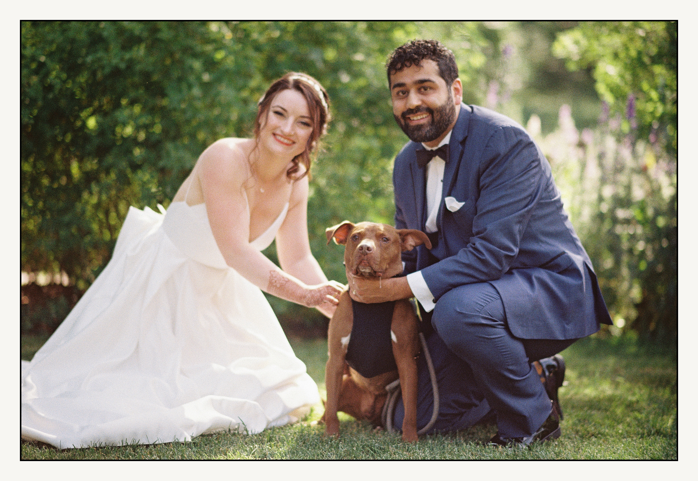 A bride and groom crouch beside their dog in Bartram's Garden.