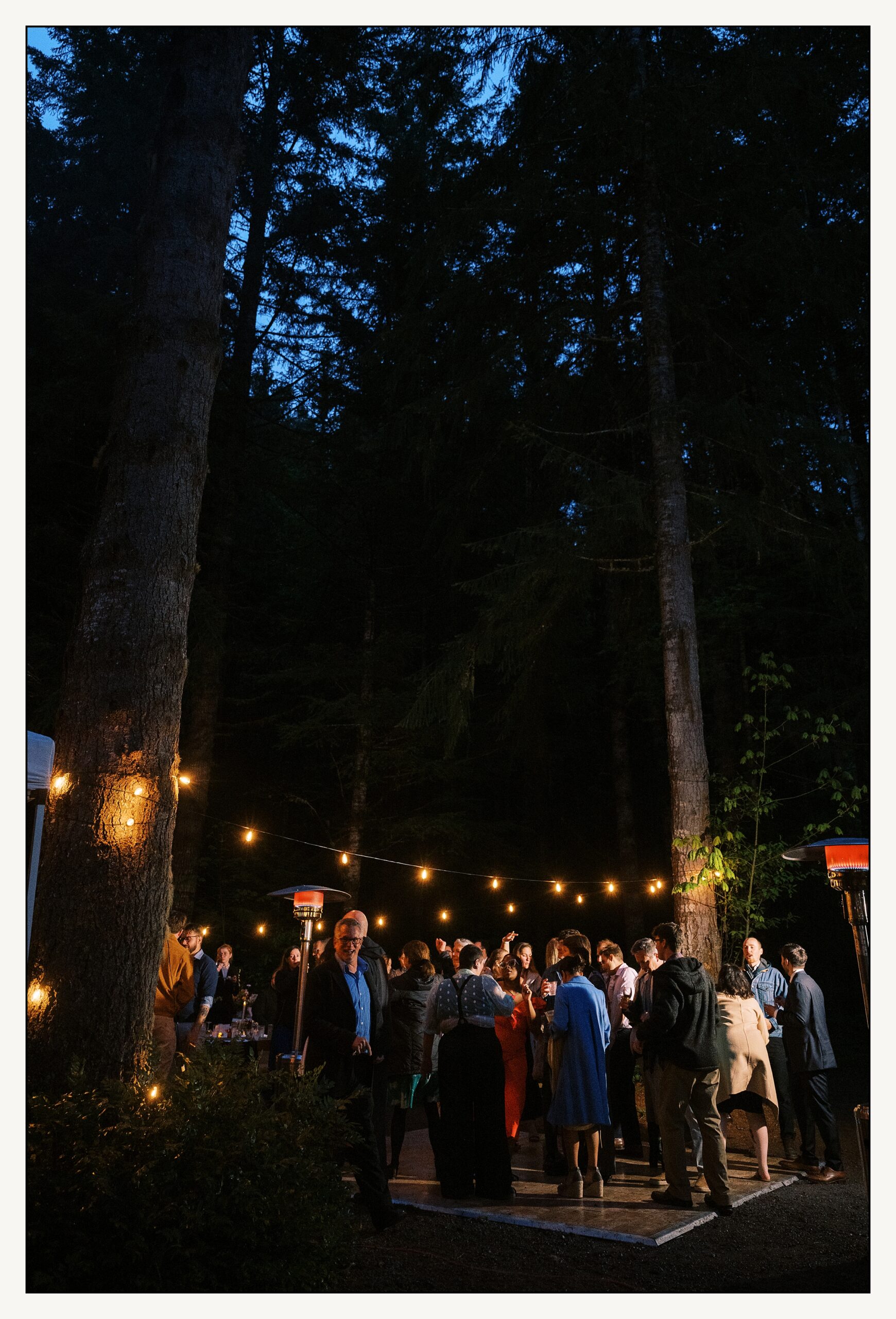 Wedding guests dance beneath strings of lights at a PNW wedding at night.