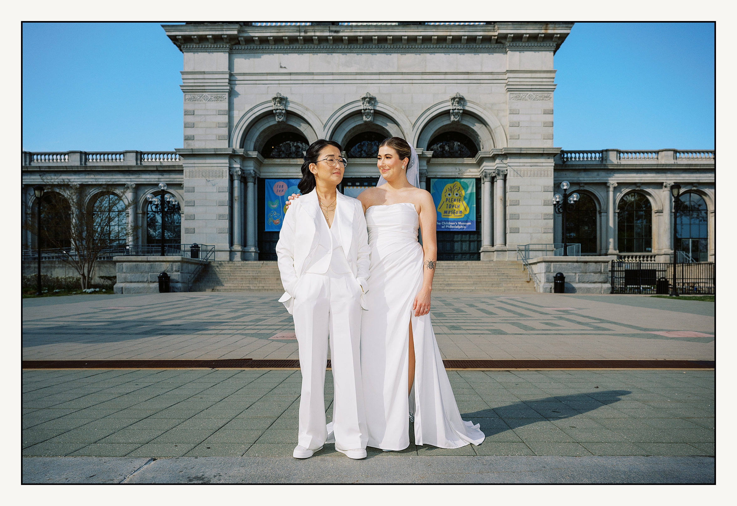 Two women in wedding clothes stand in front of a Philadelphia museum before their Please Touch Museum wedding.