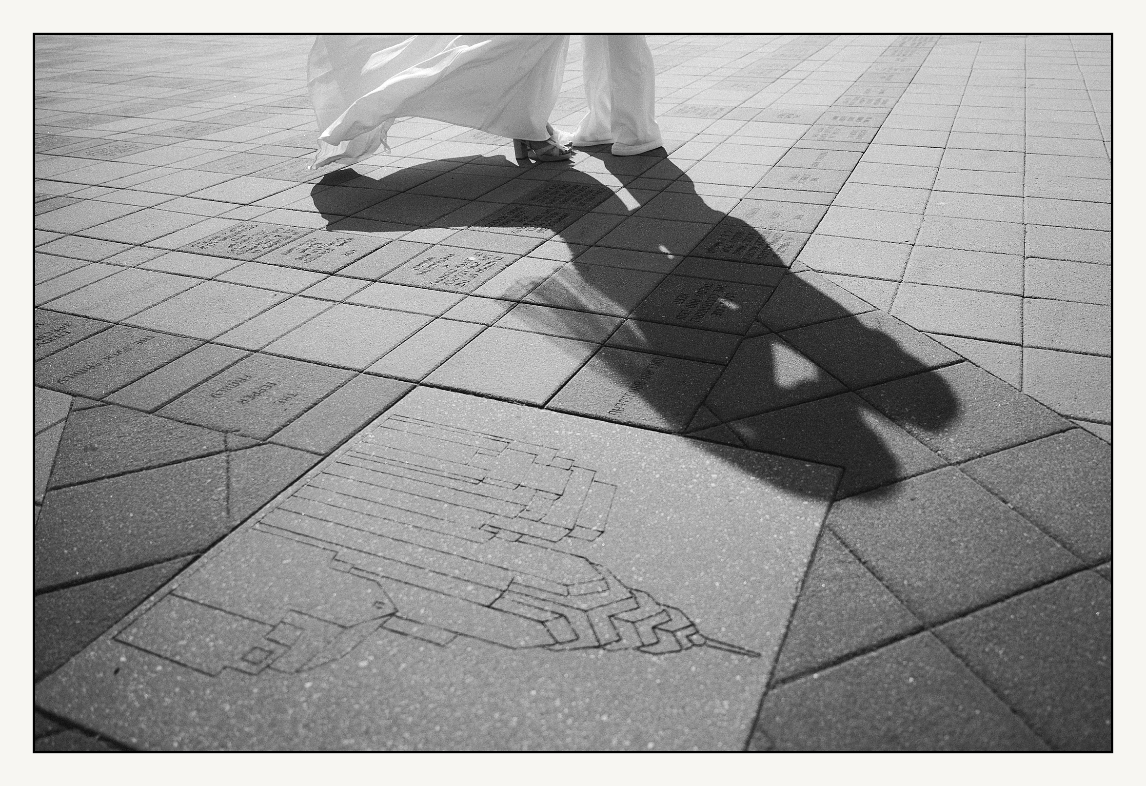 Two brides cast a shadow as they kiss on the sidewalk outside the Please Touch Museum.