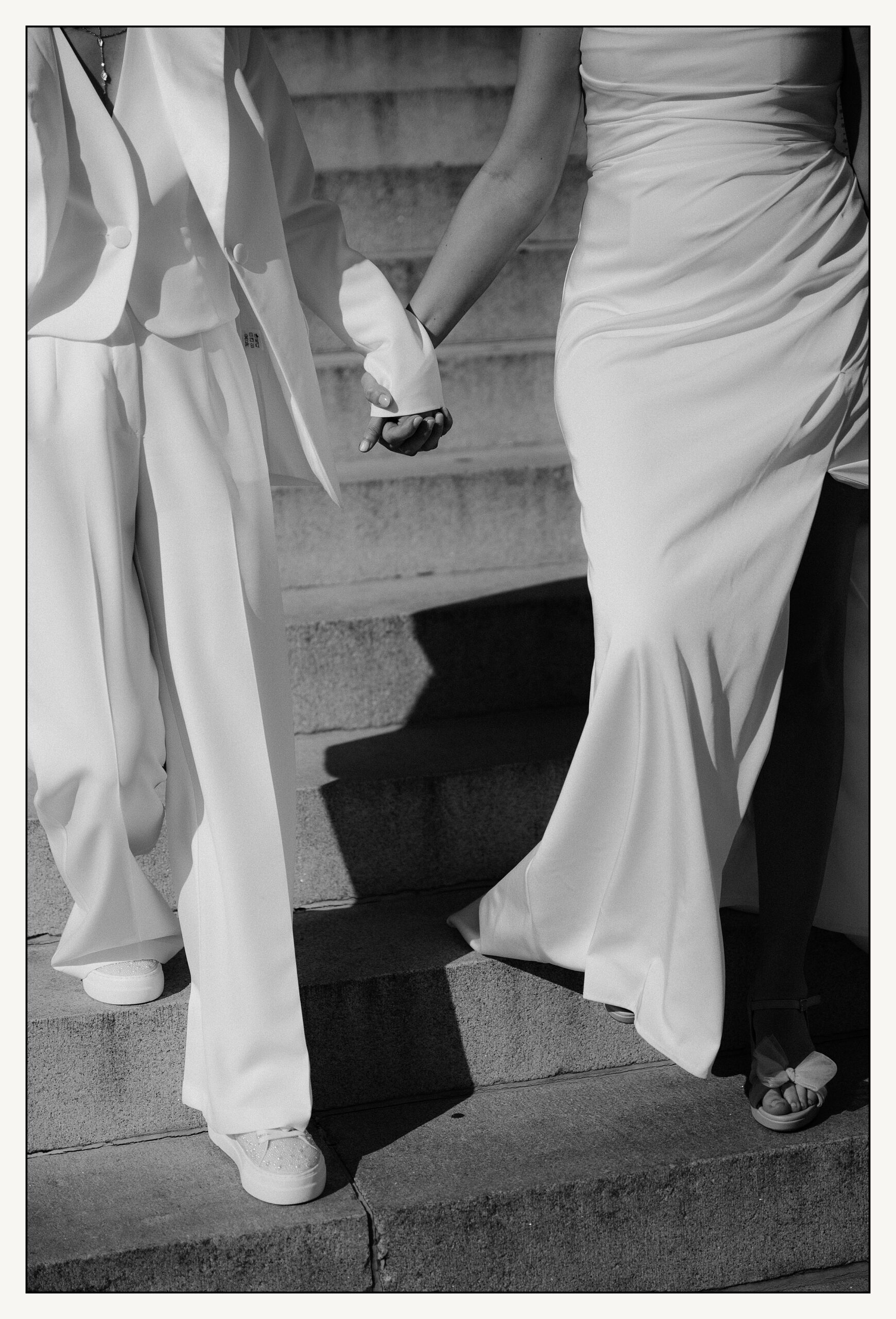 Two brides hold hands as they walk down museum steps towards a Philadelphia wedding photographer.