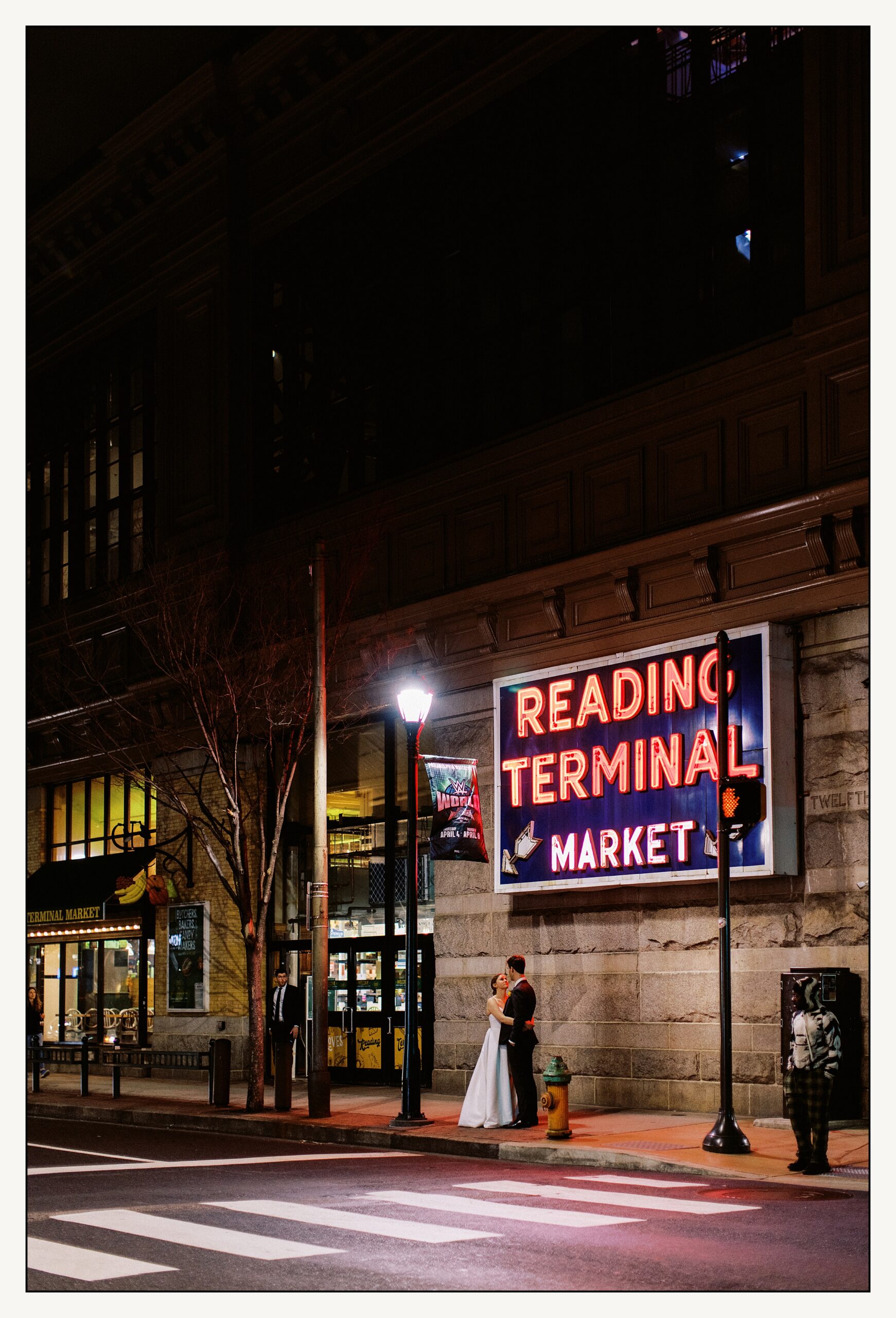 A bride and groom kiss in front of a neon sign at their Reading Terminal Market wedding.