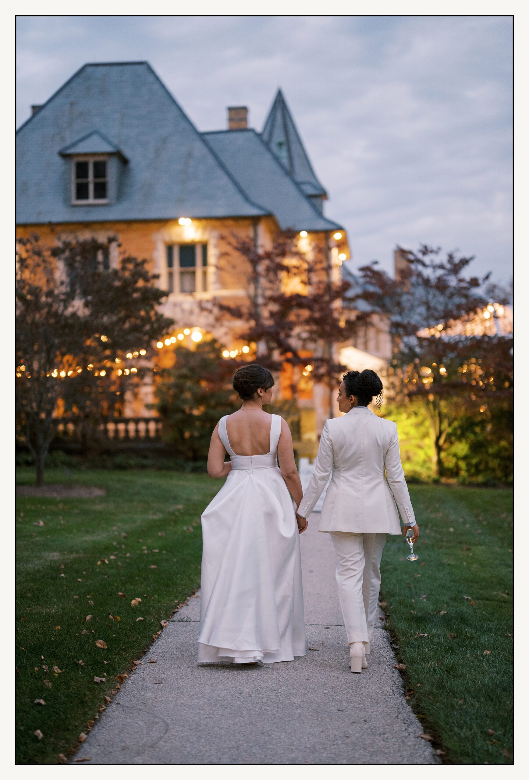 Two brides walk down a garden path towards their Cairnwood Estate wedding.